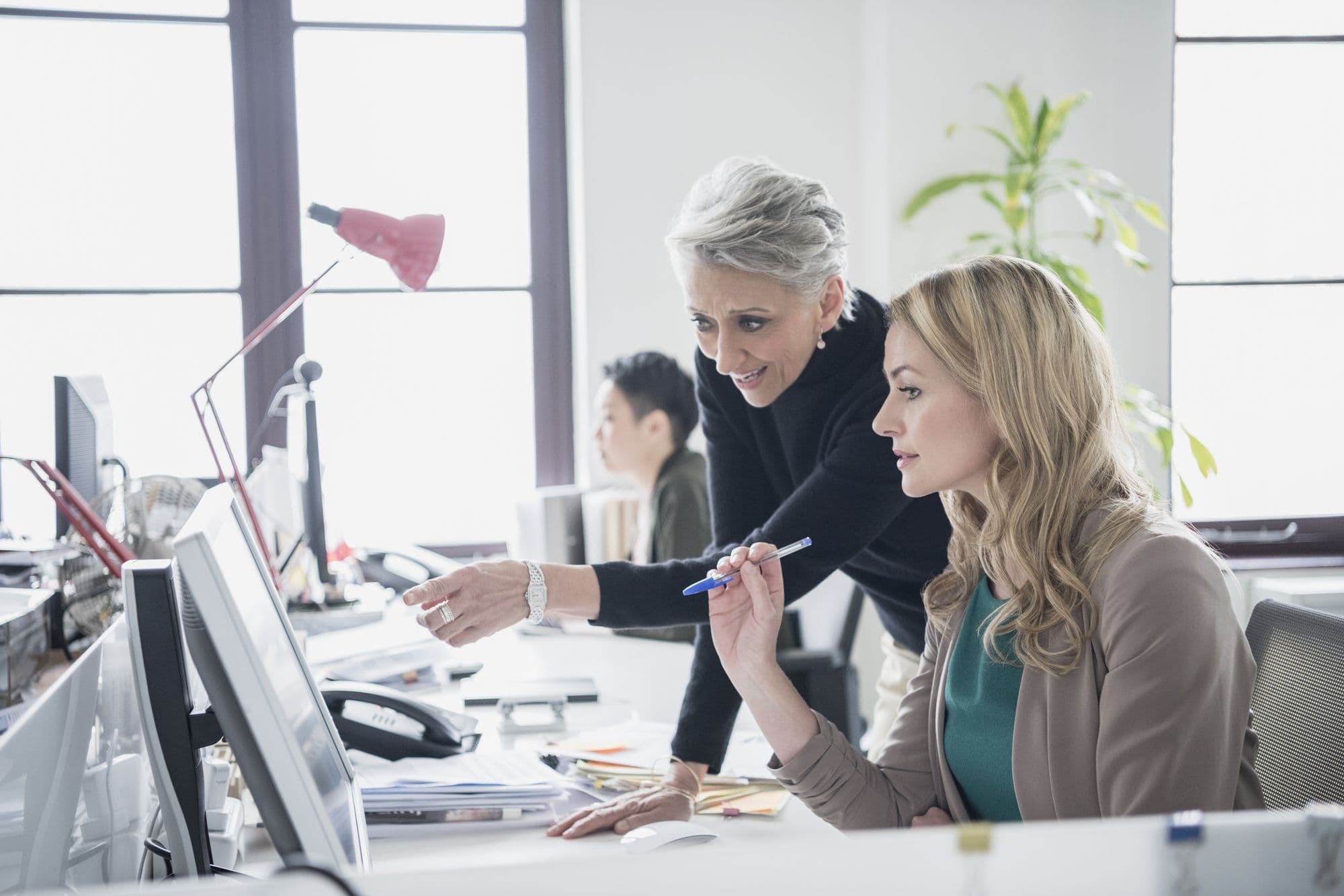 An experienced colleague guides a coworker at her screen