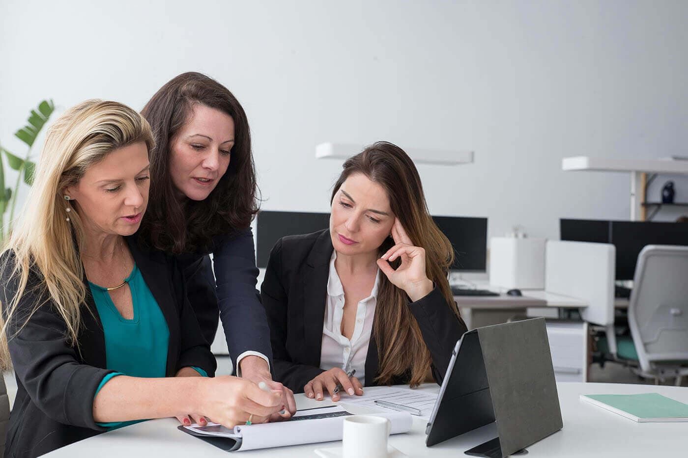 Three women review notes together at a desk