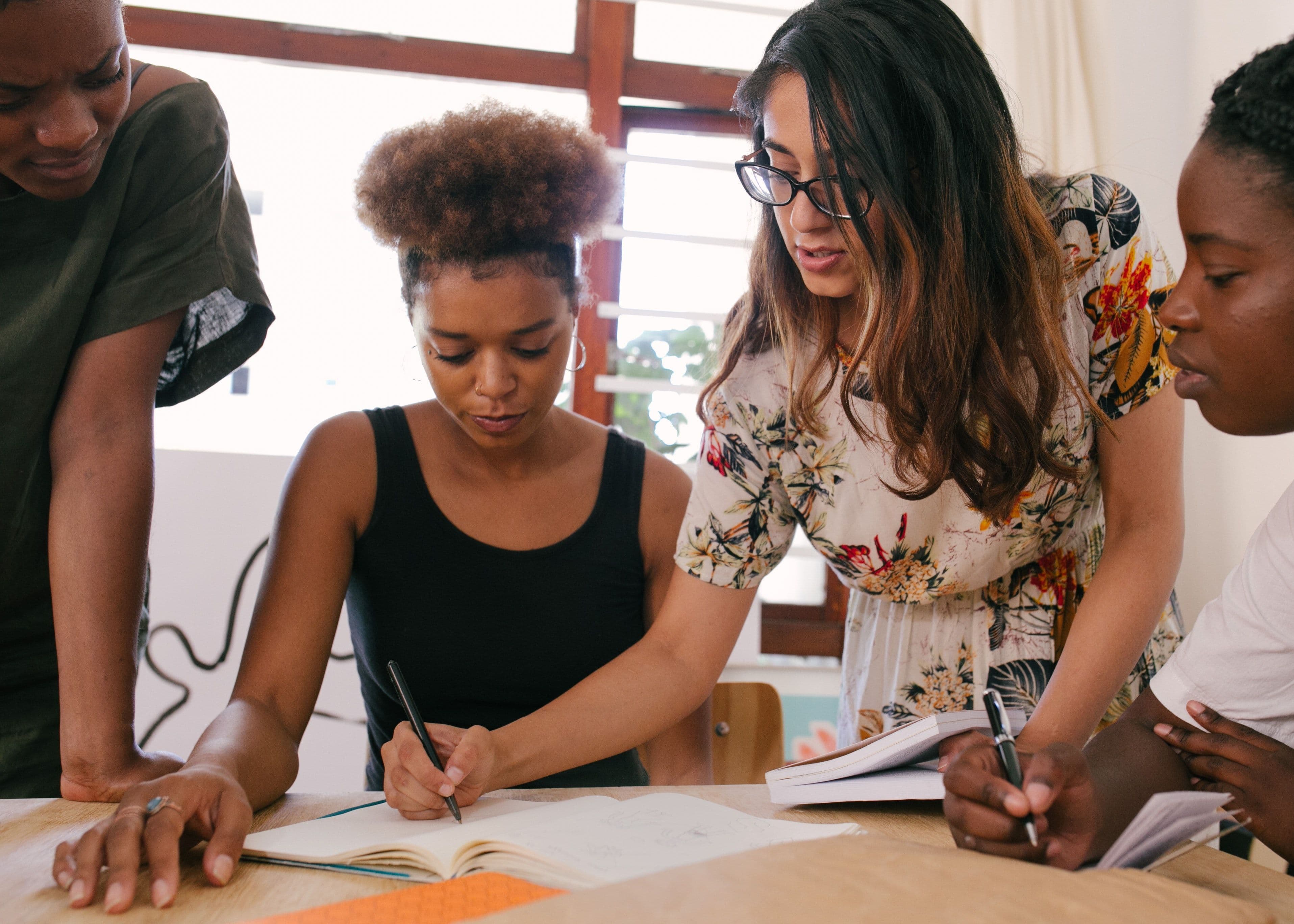 diverse female employees standing around a table during a mentoring circle meeting - mentorship program for women