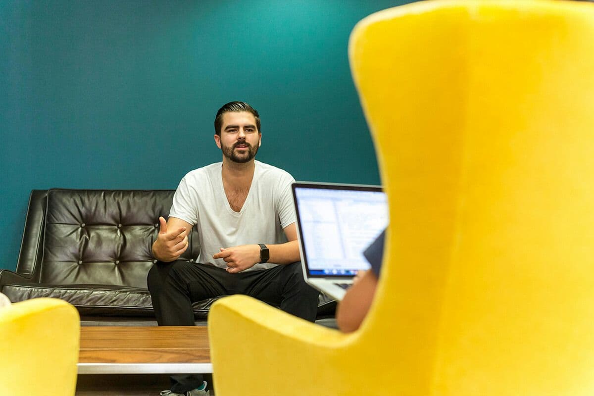 man sitting in an office talking to a colleague who is looking at their laptop discussing how to motivate their employees