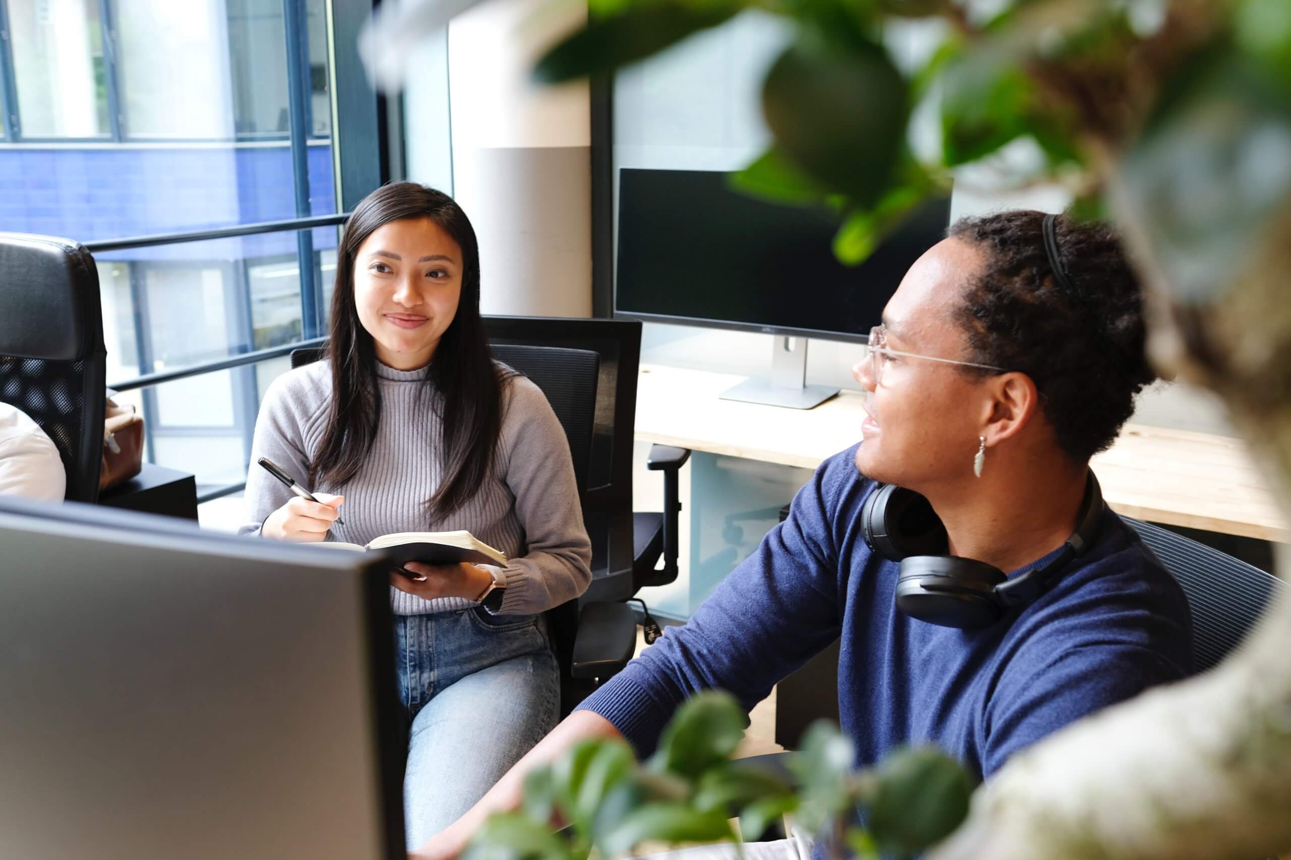 female employee takes notes in mentoring session with male coworker in the office